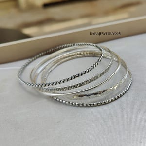 May include: Set of six silver bangles with different textures, including a twisted, a hammered, and a beaded design.  BABAJEWELRY925.