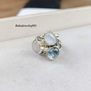 Könnte beinhalten: Eine Ansammlung von Silberringen mit verschiedenen Edelsteinbesätzen. Die Ringe zeigen ovale und runde Edelsteine in hellblauen, weißen und klaren Farbtönen. Der Text "BabaJewelry925" ist oben links sichtbar.