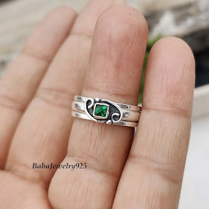 May include: A silver ring with three bands and a green gemstone in the centre. The ring is set with a delicate design.