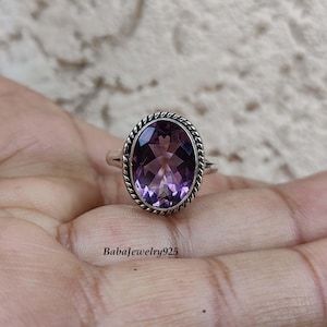 Könnte beinhalten: Ein silberner Ring mit einem großen, ovalen Amethyst-Edelstein. Der Ring hat ein gedrehtes Band und eine detaillierte Fassung um den Stein.