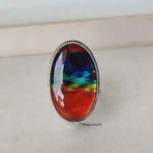 May include: A silver ring with an oval-shaped red, green, blue, and black gemstone. The gemstone has a cloudy, abstract design.