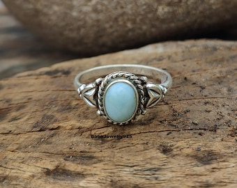 Könnte beinhalten: Ein silberner Ring mit einem hellblauen ovalen Edelstein, der in einer dekorativen silbernen Fassung sitzt. Der Ring hat ein gedrehtes Band und komplizierte Details.