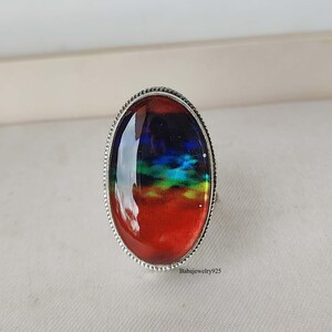May include: A silver ring with an oval-shaped red, blue, green, and black gemstone. The gemstone has a cloudy, abstract design.