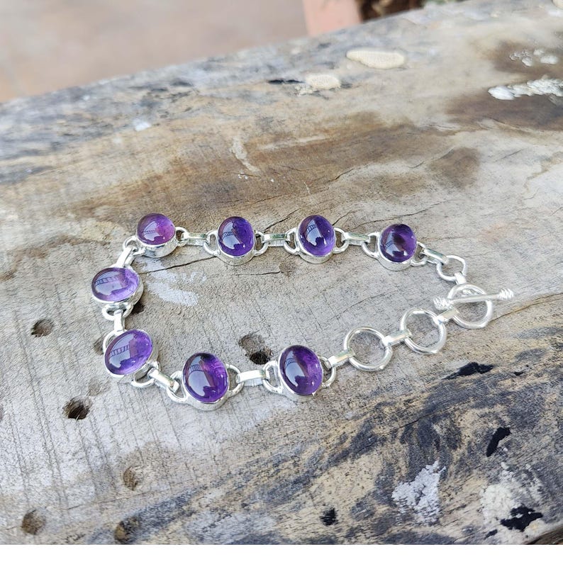 K&ouml;nnte beinhalten: Ein silbernes Kettenarmband mit ovalen Amethyst-Edelsteinen. Das Armband hat einen Schiebeverschluss.