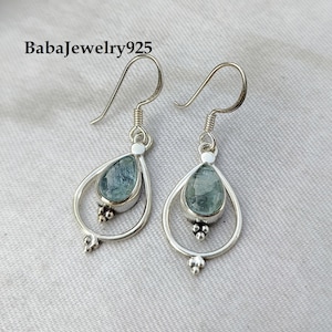 May include: A pair of silver dangle earrings with teardrop-shaped aquamarine gemstones. The earrings have a delicate, intricate design with small silver beads.