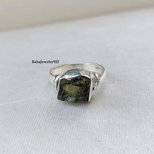 May include: A silver ring with a green gemstone. The ring has a twisted band and the gemstone is a rough cut.