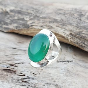 May include: A silver ring with a green oval gemstone. The ring has a unique, open design.