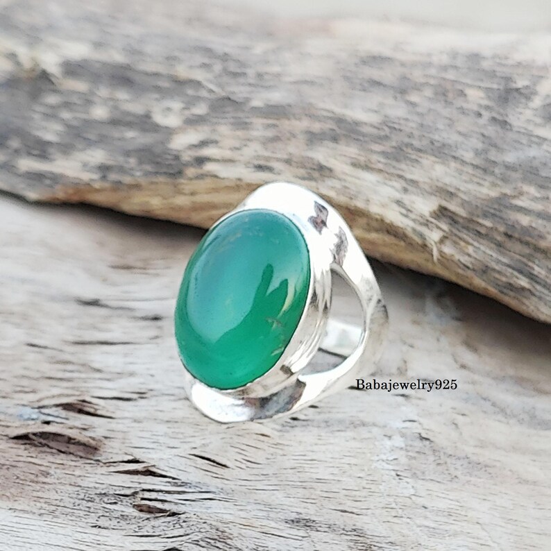 May include: A silver ring with a green oval gemstone. The ring has a unique, open design.