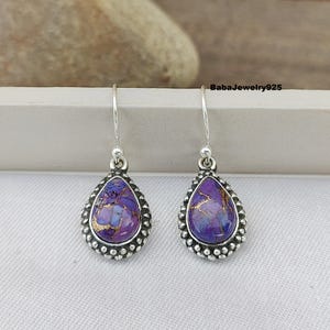 May include: A pair of silver dangle earrings with purple and gold gemstone drops. The earrings have a beaded border around the gemstone.