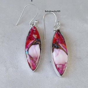 May include: A pair of silver dangle earrings with a pink, red, and brown marbled stone. The stones are oval shaped and have a silver setting.