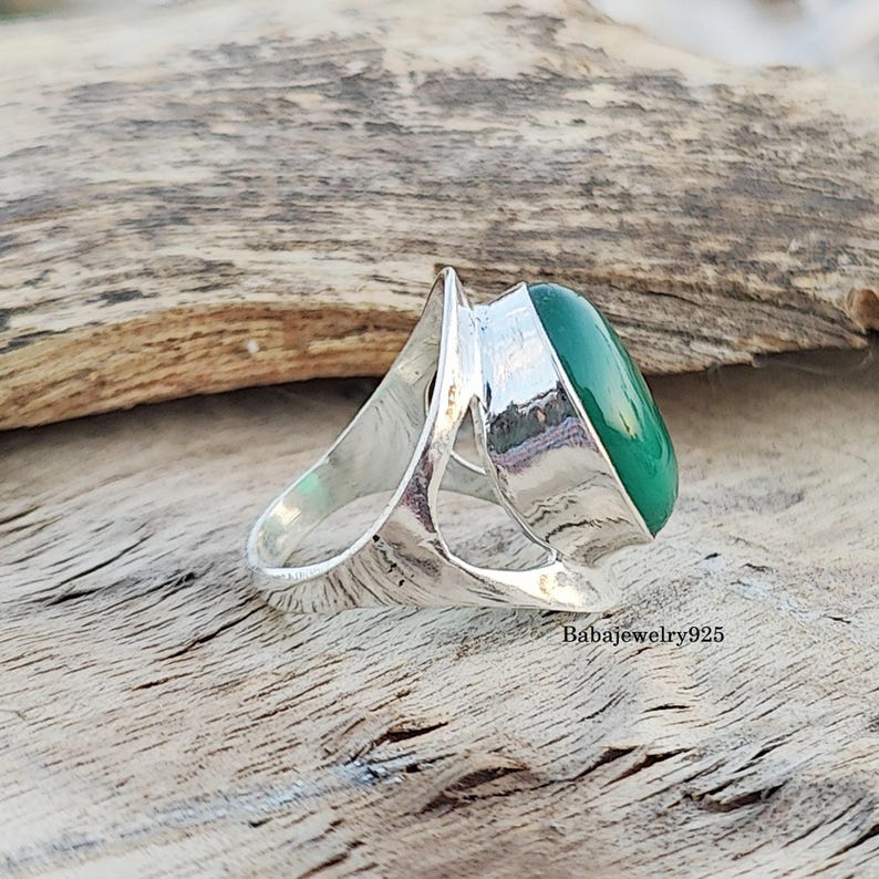May include: A silver ring with a large, oval-shaped green gemstone set in a unique, open-work design.