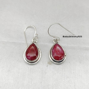 May include: A pair of silver dangle earrings with teardrop-shaped red ruby gemstones. The earrings have a simple design and are perfect for everyday wear.