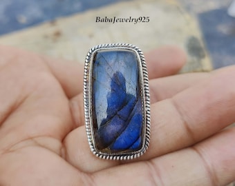 Può includere: Un anello d'argento con una grande pietra rettangolare di labradorite blu. L'anello ha un design a corda attorno al bordo dell'incastonatura.