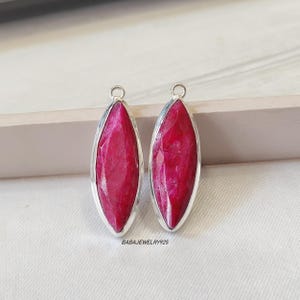 May include: Two silver pendant charms with a red gemstone in the shape of a marquise. The gemstone is faceted and has a shiny finish.