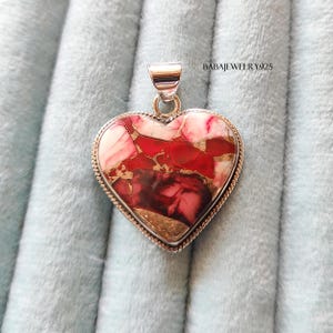 May include: A silver heart-shaped pendant with a red, white, and gold marbled stone. The pendant is on a blue velvet background.  BABAJEWELRY925