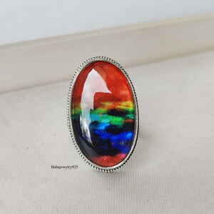 May include: A silver ring with an oval-shaped, rainbow-colored glass stone. The stone has a red, orange, yellow, green, blue, and purple color scheme.