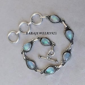 May include: A silver bracelet with a toggle clasp features six teardrop-shaped iridescent stones set in silver.