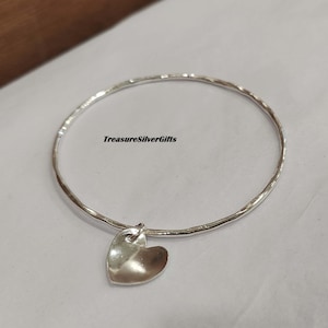 Puede incluir: Un brazalete de plata con acabado martillado y un pequeño dije en forma de corazón.