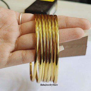 May include: A set of seven gold-coloured metal bangles. The bangles are stacked on top of each other and are all the same size and width.