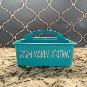 May include: A turquoise plastic storage bin with a handle and the text "BABY MAKIN' STATION" printed on the front.