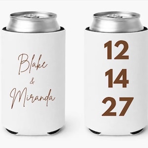 May include: White can cooler with a brown top and bottom. The front features the names "Blake & Miranda" in a cursive font. The back displays the numbers "12 14 27" in a bold, brown font. The can cooler is designed to keep beverages cold.