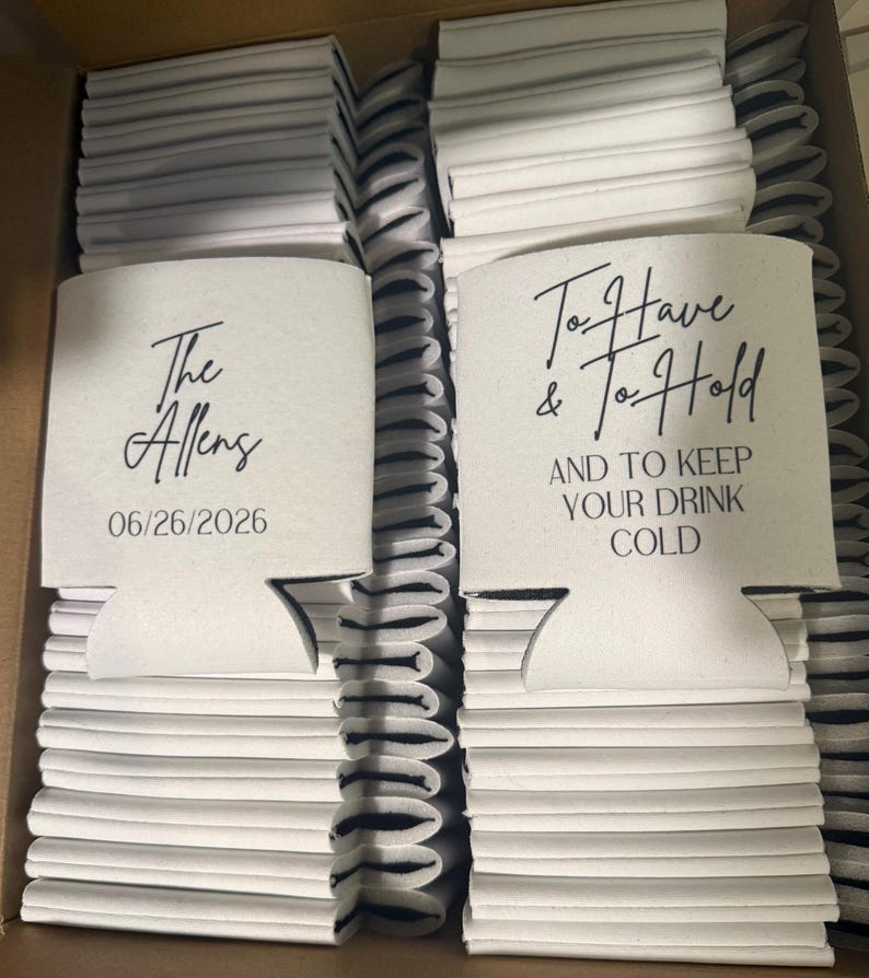 May include: A large collection of white foam can coolers stacked in a box. One cooler features the text The Allens and 06/26/2026. Another cooler displays the text To Have & To Hold AND TO KEEP YOUR DRINK COLD in black script and block lettering.