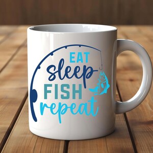 Puede incluir: Taza de cerámica blanca con las palabras "Eat Sleep Fish Repeat" en letras azules y turquesas. Un gráfico de caña de pescar y una ilustración de pez también aparecen en la taza. La taza tiene un asa curva y está sobre una superficie de madera.
