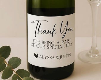 May include: A green wine bottle with a white label that reads "Thank You" in elegant script. Below, it says "For being a part of our special day" and "Alyssa & Justin". A black heart is also on the label.