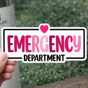 May include: A rectangular sticker with the words "EMERGENCY DEPARTMENT" in pink and white, with a pink heart above the word "EMERGENCY". The sticker has a black border and is held in a person's hand.