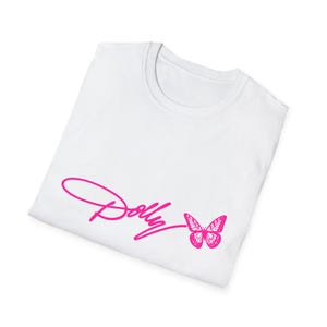 May include: A white short-sleeved t-shirt featuring a bright pink graphic print on the front. The design consists of the word Dolly written in a cursive script font, followed by a detailed illustration of a butterfly in the same pink color.