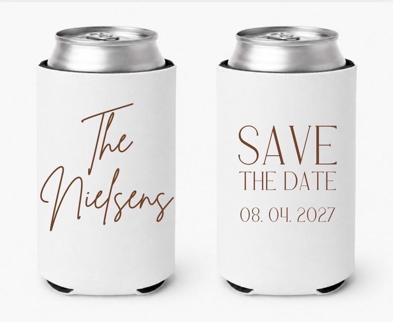 May include: Two white can coolers with brown text. One says "The Nielsens" in cursive, the other says "SAVE THE DATE 08.04.2027". The cans are silver and the coolers have black bottoms.