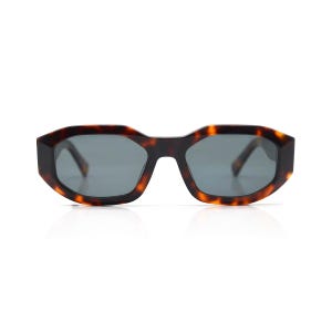 Può includere: Occhiali da sole tartaruga con montatura geometrica e lenti grigie scure.