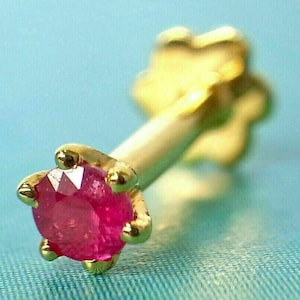 Op de afbeelding: Een gouden neuspiercing met een kleine, ronde, roze robijn.