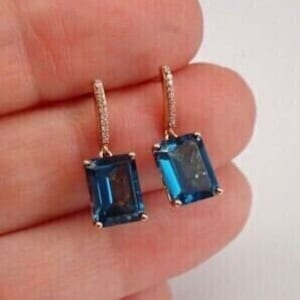 May include: A pair of dangle earrings with a blue topaz gemstone and a diamond accent. The earrings are made of rose gold.
