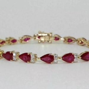 May include: A gold bracelet featuring a line of pear-shaped ruby gemstones with smaller diamond accents.