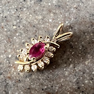Może przedstawiać: Złoty wisiorek z różowym owalnym kamieniem szlachetnym otoczonym mniejszymi przezroczystymi kamieniami szlachetnymi.