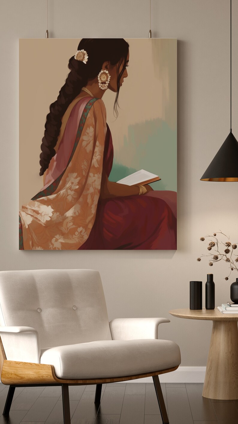 May include: An art print showing a woman in traditional Indian dress, seated and reading a book. The artwork uses burgundy, peach, and gold tones, with detailed jewellery and clothing. The print hangs above a white armchair.