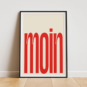 May include: A framed print with a cream background and the word "moin" in bold, red letters.