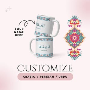 May include: Two white ceramic mugs stacked on top of each other, each with a handle. The mugs feature Arabic script and the name "Tabitha" in English. The mugs have a decorative floral border in blue, red, and green. The word "Customize" is below the mugs.