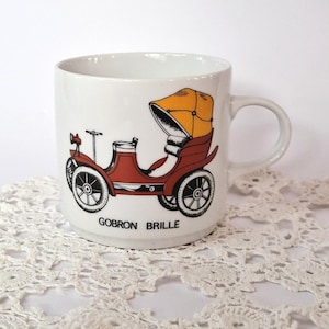 Peut inclure: Une tasse en céramique blanche avec une illustration rouge et jaune d'une voiture vintage Gobron-Brillie. La tasse a une poignée noire.