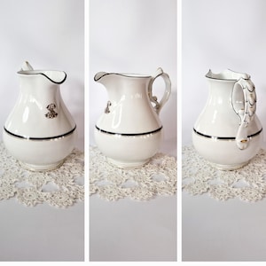 May include: White porcelain creamer with a black and gold trim. The creamer has a rounded body and a handle with a decorative design.