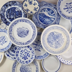 Może przedstawiać: Kolekcja białych ceramicznych talerzy i misek z różnymi niebieskimi wzorami transferowymi, w tym sielankowymi krajobrazami, motywami kwiatowymi i geometrycznymi obwódkami. Asortyment obejmuje okrągłe i kwadratowe kształty ze szczegółowymi wzorami.