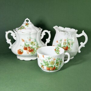 Peut inclure: Un service à thé en porcelaine blanche avec un motif de fraises et de fleurs. L'ensemble comprend un sucrier avec un couvercle, un pot à crème et une tasse.