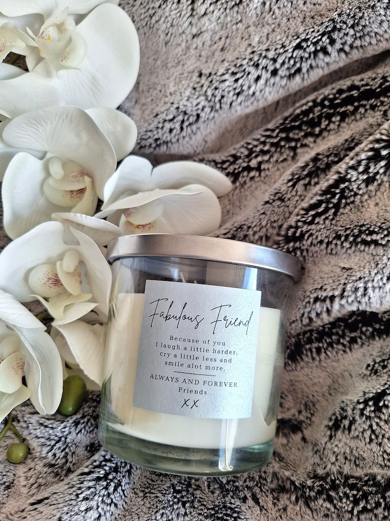 May include: A white candle in a clear glass jar with a silver lid. The label on the jar reads "Fabulous Friend" and includes the text "Because of you I laugh a little harder, cry a little less and smile a lot more. Always and Forever Friends XX".