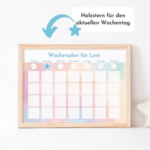 Puede incluir: Un cuadro semanal de tareas enmarcado con un fondo de acuarela en tonos rosa, naranja y azul. El cuadro est&aacute; etiquetado como "Wochenplan f&uuml;r Leni" y tiene espacios para cada d&iacute;a de la semana. Una estrella azul se coloca en el espacio del martes. Una flecha azul apunta a una estrella sobre el cuadro, con el texto "Holzstern f&uuml;r den aktuellen Wochentag".