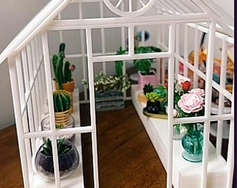 May include: A white miniature greenhouse with a glass roof and a white metal frame. The greenhouse is filled with small potted plants, including succulents and flowers.