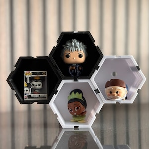 Peut inclure: Une étagère hexagonale noire et blanche contenant plusieurs figurines. L'étagère contient un Funko Pop de la Princesse Minnie, une figurine d'une femme aux cheveux gris, une figurine de Tiana et une figurine d'un vieil homme.