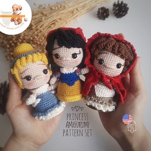 Puede incluir: Tres muñecas de princesa de ganchillo hechas a mano: Cenicienta con un vestido azul, Blancanieves con un vestido amarillo y Caperucita Roja con una capa roja. Las muñecas forman parte de un conjunto de patrones de Amigurumi de Princesas. Las muñecas están en las manos de una persona.