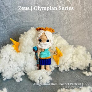 May include: A crocheted amigurumi doll of Zeus from the Olympian Series, featuring a white beard, gold crown, turquoise tunic, and blue skirt. The doll holds a brown staff with a blue top and a yellow lightning bolt, surrounded by white fluff.