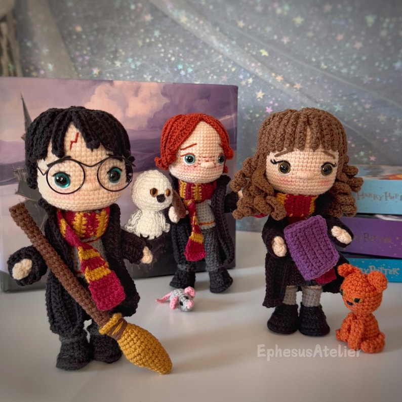 Pode incluir: Tr&ecirc;s personagens de Harry Potter feitos de croch&ecirc;, Harry Potter, Ron Weasley e Hermione Granger, com seus respectivos companheiros animais. Harry Potter est&aacute; segurando uma vassoura, Ron Weasley est&aacute; segurando um rato e Hermione Granger est&aacute; segurando um gato. Os personagens est&atilde;o todos usando seus uniformes de Hogwarts.